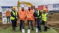 Group of people at the groundbreaking ceremony for the next phase of Airfield Business Park, holding shovels and standing on a construction site.